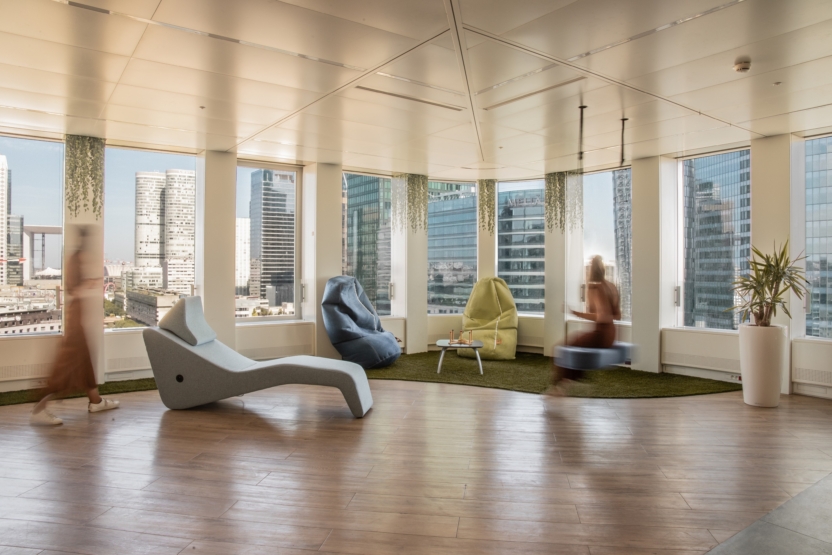 Espace détente lumineux avec fauteuils design et vue sur les tours de bureaux.