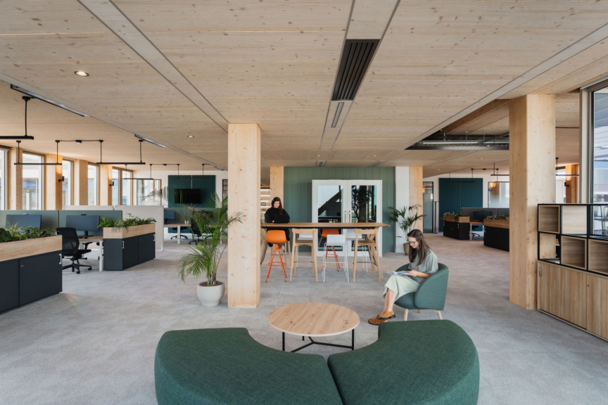 Espace de travail DKV conçu par ARCH.DESIGN, au style architectural moderne avec mobilier en bois clair, assises vertes et ambiance lumineuse.