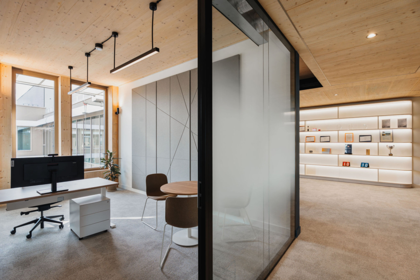 Bureau vitré DKV conçu par ARCH.DESIGN avec espace d’exposition intégré et éclairage chaleureux.