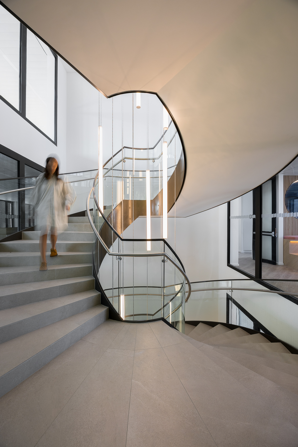 Escalier design aux lignes courbes et éclairage intégré, élément central reliant les étages du siège Tristan Capital Partners